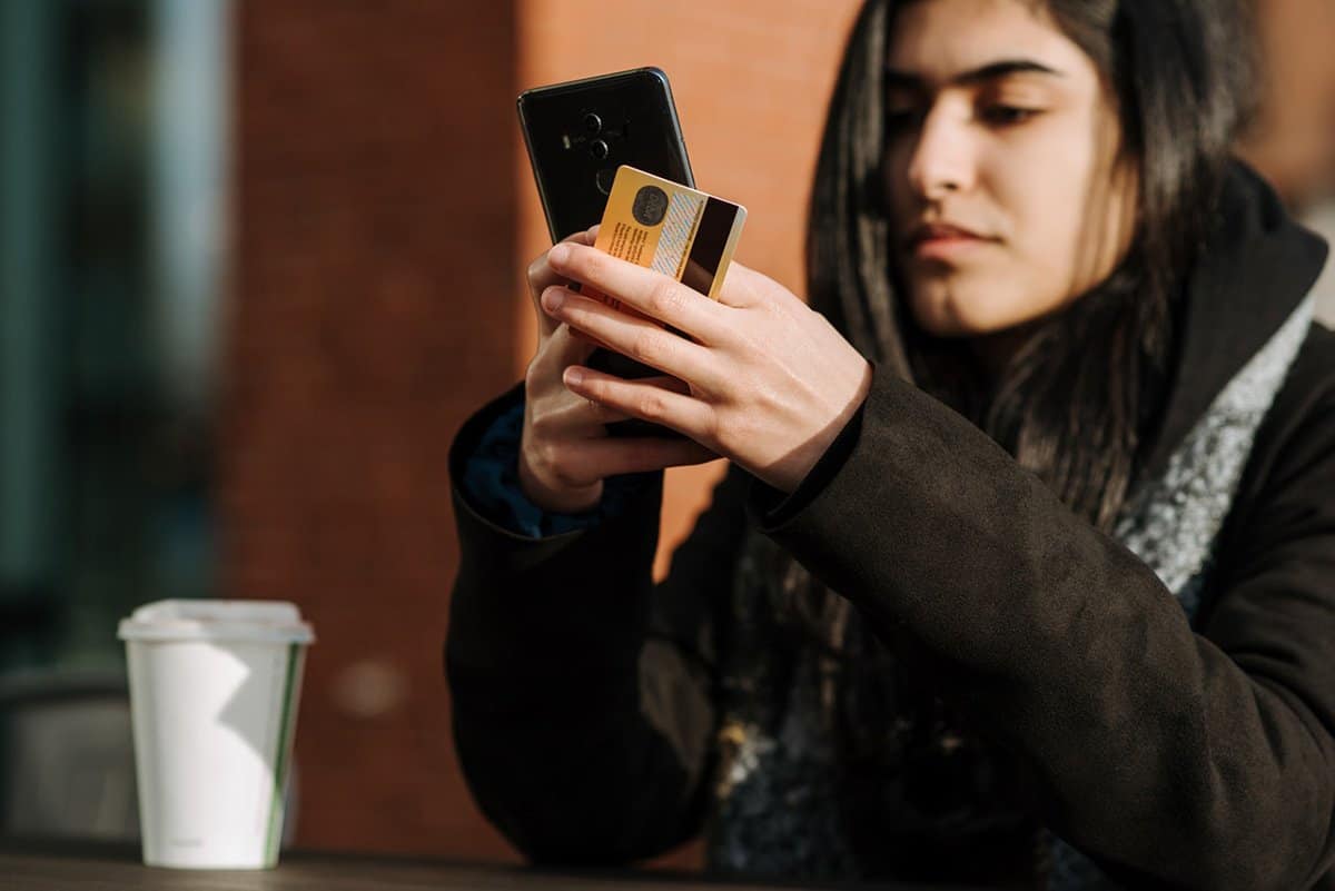 person holding credit card and mobile phone with coffee