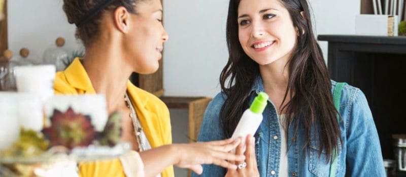 Two women discussing a lotion in a retail location.