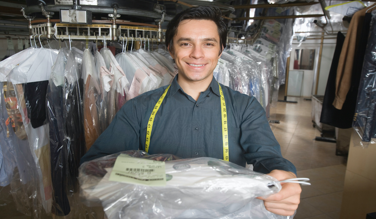 Administrator at dry cleaners keeps clean clothes on hangers in bag, Stock  image